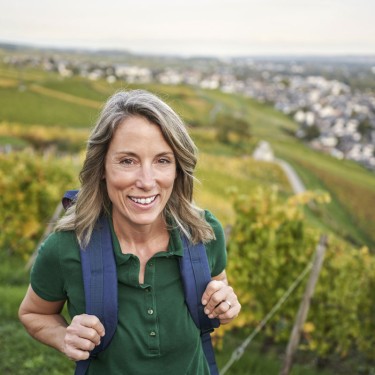 Woman with backpack standing on hill overlooking vineyards, river, and town