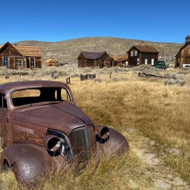 Rusty antique car in field with buildings in background Bodie State Historic Park