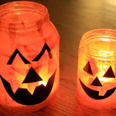 Handmade Halloween pumpkin votive lanterns created from recycled glass jars, orange tissue paper, and black jack-o'-lantern faces.