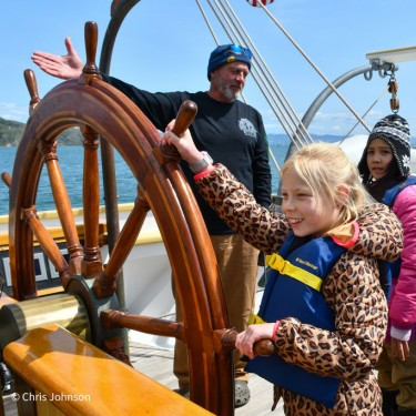 Kids in summer sailing camp steering boat with instructor