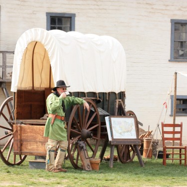 Man in historical costume standing beside a covered wagon at Sutter's Fort State Historic Park