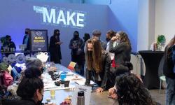 Several people standing and talking, and sitting at a table with art supplies