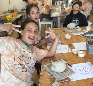 Three students smiling and having fun while creating pottery pieces in ceramic class at Studio 4 Art