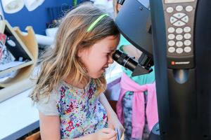 Young girl looking at the moon through a telescope. 