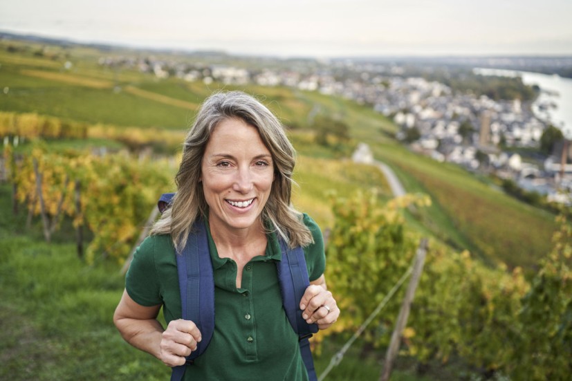 Woman with backpack standing on hill overlooking vineyards, river, and town