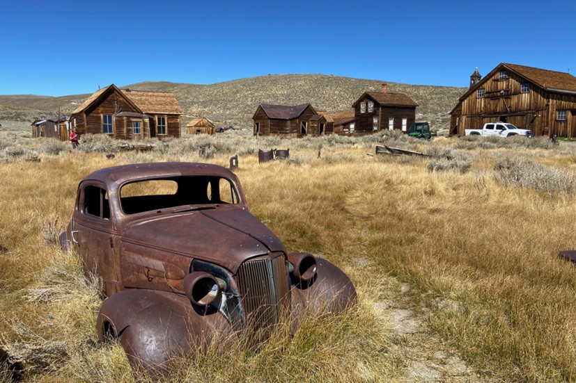 Rusty antique car in field with buildings in background Bodie State Historic Park