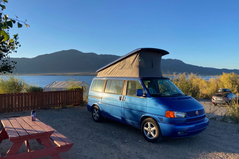Campground by lake with blue VW camper and picnic table