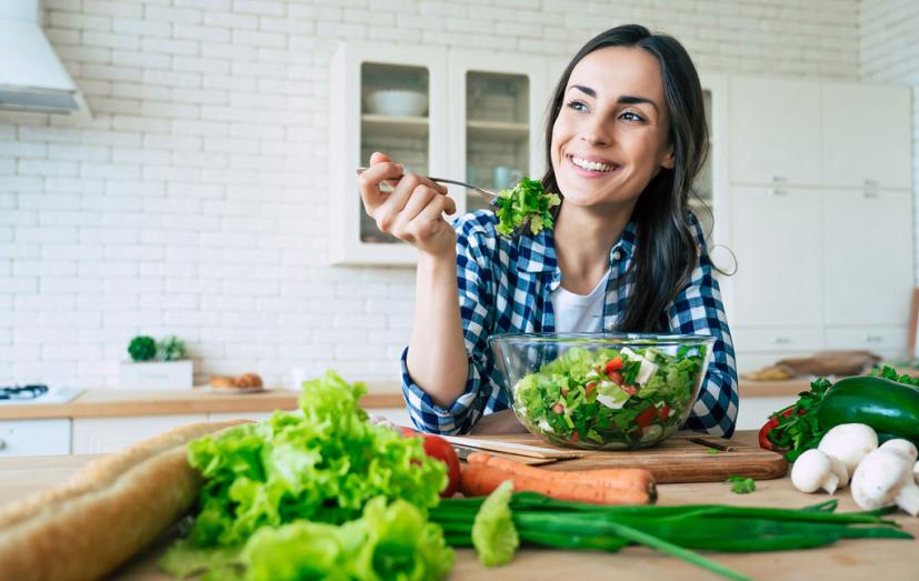 Woman eating salad surrounded by vegetables