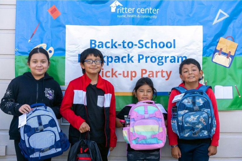 Kids with school backpacks in front of sign for school supply campaign
