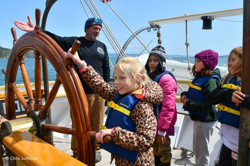 Kids in summer sailing camp steering boat with instructor