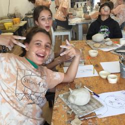 Three students smiling and having fun while creating pottery pieces in ceramic class at Studio 4 Art