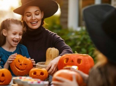 Woman in witch costume and girls at table with pumpkin