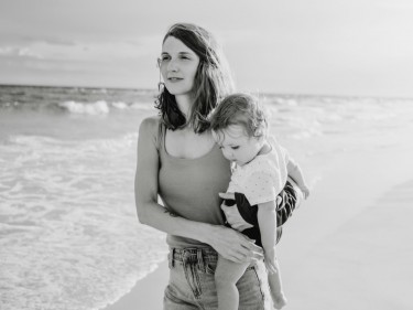 Black and white photo of mom on beach holding toddler