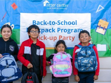 Kids with school backpacks in front of sign for school supply campaign