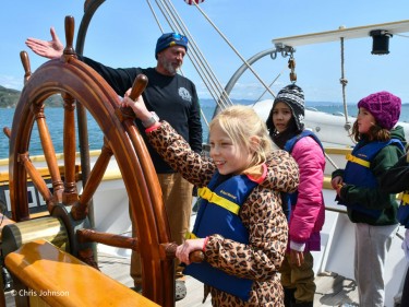 Kids in summer sailing camp steering boat with instructor