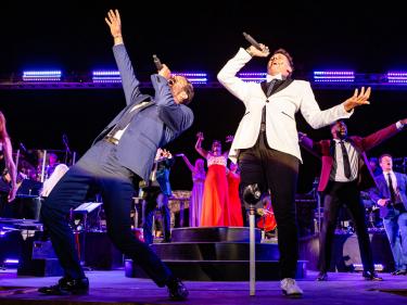 Broadway performers singing and dancing on outdoor stage